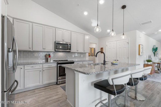 kitchen featuring a center island with sink, appliances with stainless steel finishes, tasteful backsplash, decorative light fixtures, and sink