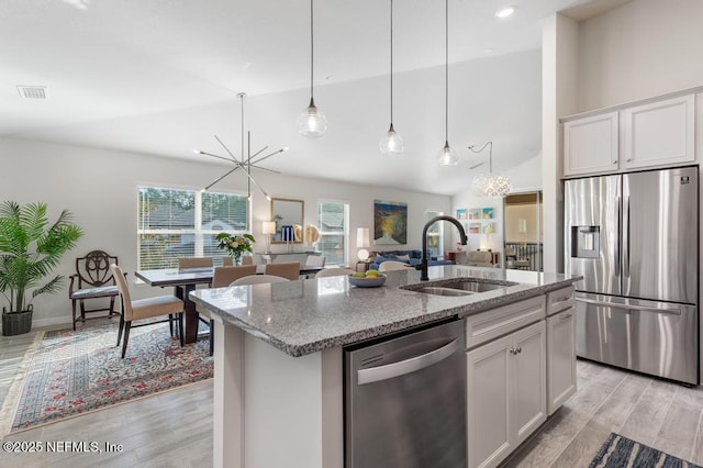 kitchen featuring a center island with sink, sink, white cabinetry, light stone countertops, and stainless steel appliances