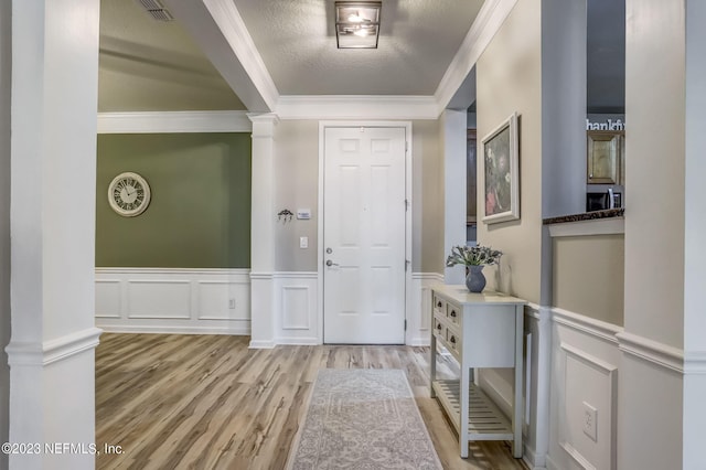 foyer featuring light wood-type flooring, decorative columns, a textured ceiling, and ornamental molding