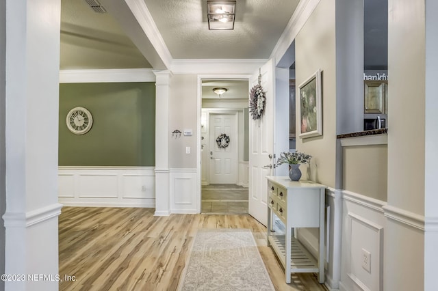 corridor featuring a textured ceiling, crown molding, light hardwood / wood-style flooring, and decorative columns