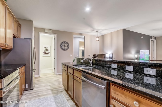 kitchen with light hardwood / wood-style floors, stainless steel appliances, dark stone countertops, hanging light fixtures, and sink