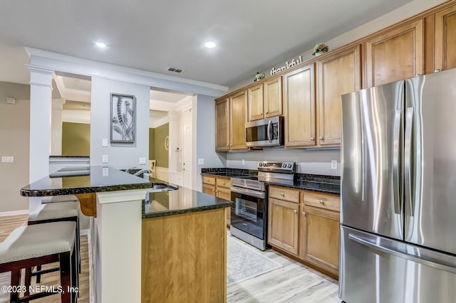 kitchen with appliances with stainless steel finishes, light wood-type flooring, a kitchen breakfast bar, dark stone countertops, and sink