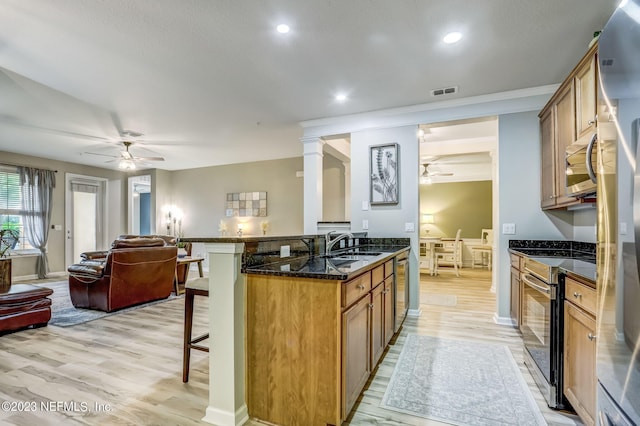 kitchen with a kitchen bar, light wood-type flooring, appliances with stainless steel finishes, dark stone counters, and ornate columns