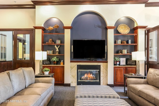 living room with built in shelves, a tile fireplace, dark carpet, and ornamental molding