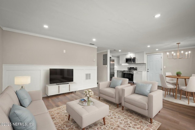 living room featuring light wood-type flooring, a notable chandelier, ornamental molding, and electric panel