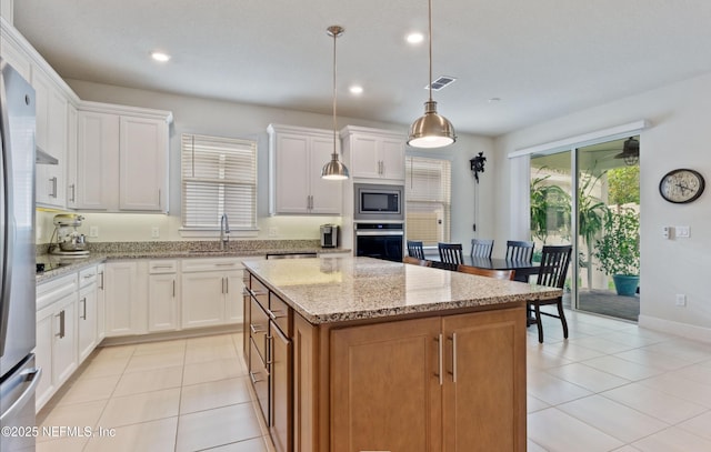 kitchen featuring light stone countertops, pendant lighting, stainless steel appliances, a kitchen island, and white cabinetry