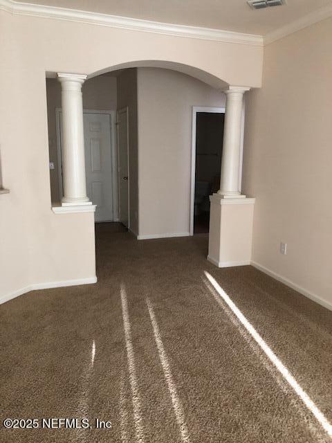 unfurnished room featuring ornate columns, crown molding, and dark carpet