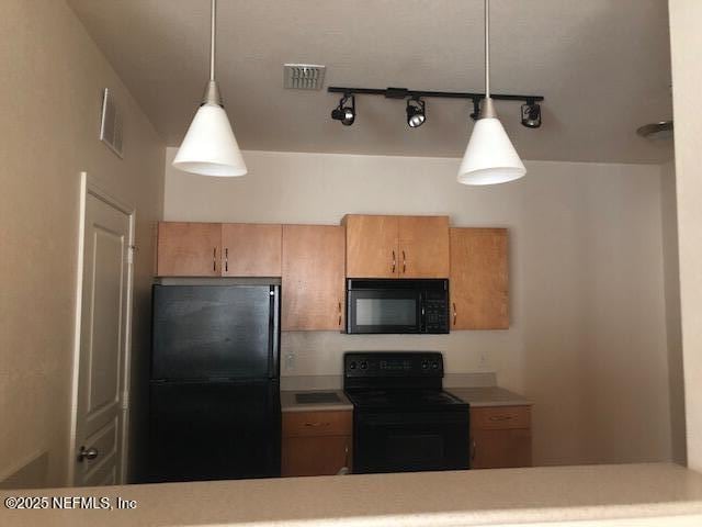 kitchen with light brown cabinets, hanging light fixtures, and black appliances