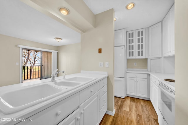 kitchen with white appliances, sink, light hardwood / wood-style floors, and white cabinets