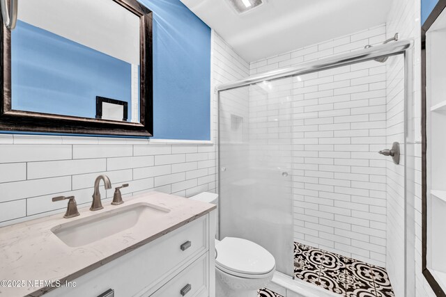 bathroom featuring vanity, toilet, a shower with shower door, and tile walls