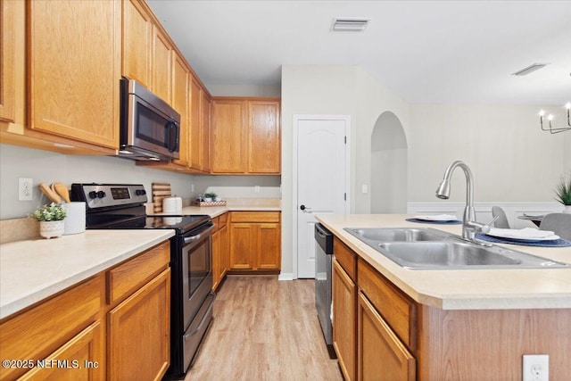 kitchen with stainless steel appliances, a notable chandelier, light wood-type flooring, a kitchen island with sink, and sink