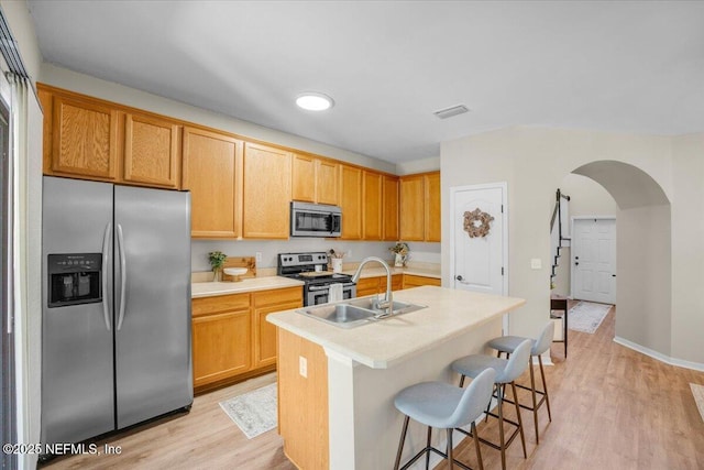 kitchen with stainless steel appliances, sink, light hardwood / wood-style flooring, a center island with sink, and a breakfast bar