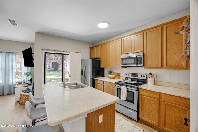 kitchen with a kitchen island with sink, stainless steel appliances, light wood-type flooring, a breakfast bar, and sink