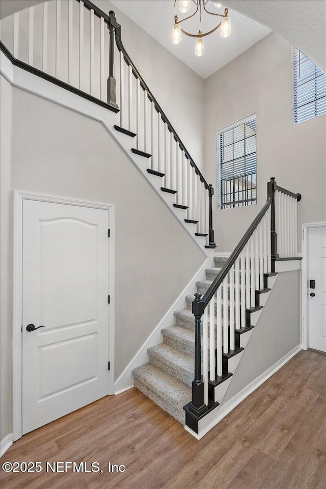 staircase with a high ceiling, a chandelier, and wood-type flooring