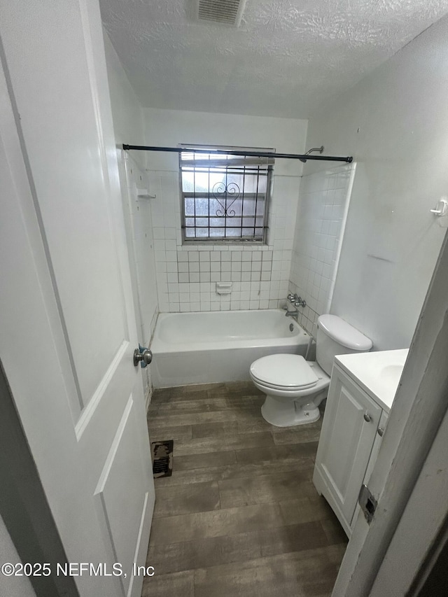 full bathroom with hardwood / wood-style floors, a textured ceiling, tiled shower / bath combo, vanity, and toilet