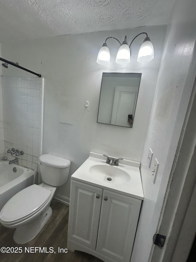 full bathroom with toilet, tiled shower / bath combo, wood-type flooring, a textured ceiling, and vanity