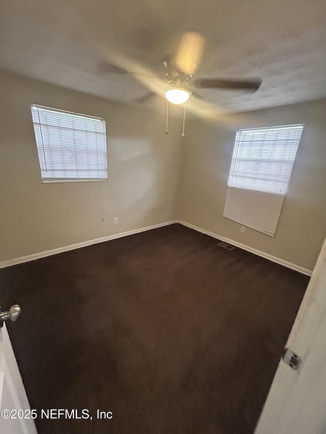 unfurnished room featuring ceiling fan, dark carpet, and a wealth of natural light