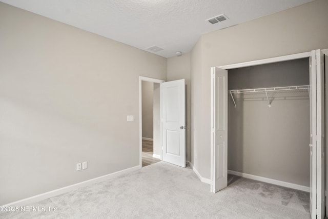 unfurnished bedroom featuring a textured ceiling, a closet, and light carpet