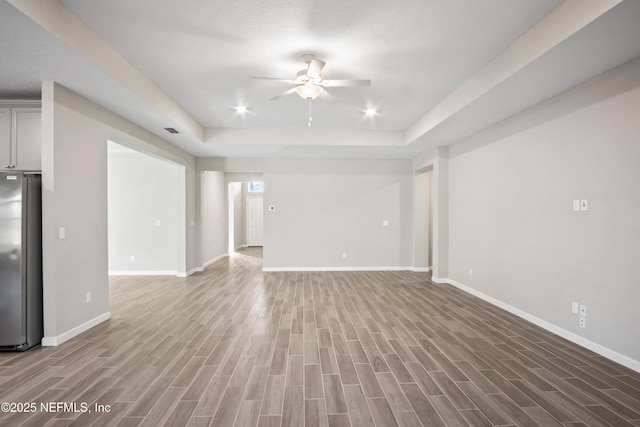 unfurnished living room with a raised ceiling, ceiling fan, and wood-type flooring