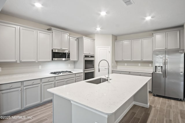 kitchen featuring a kitchen island with sink, sink, light stone counters, and stainless steel appliances