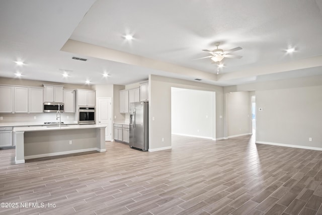 kitchen with ceiling fan, a raised ceiling, white cabinetry, a kitchen island with sink, and appliances with stainless steel finishes