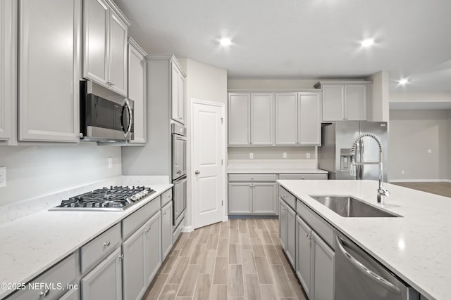 kitchen featuring gray cabinets, stainless steel appliances, light stone counters, and sink