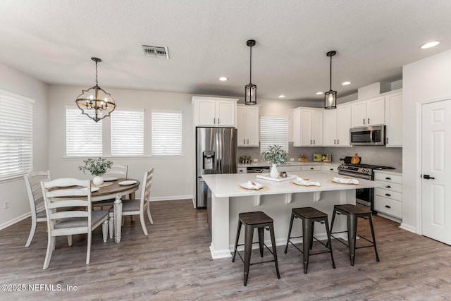 kitchen with appliances with stainless steel finishes, white cabinets, decorative light fixtures, and a center island