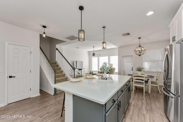 kitchen featuring ceiling fan with notable chandelier, white cabinets, a center island, stainless steel refrigerator, and light hardwood / wood-style flooring