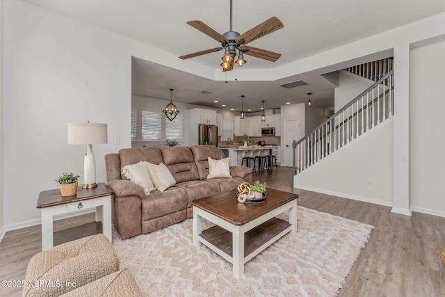 living room featuring ceiling fan with notable chandelier, a textured ceiling, and light wood-type flooring