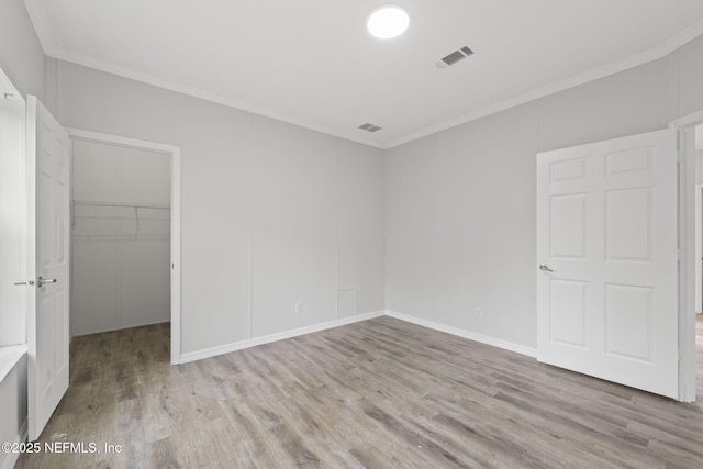 unfurnished bedroom featuring crown molding, light wood-type flooring, a closet, and a spacious closet