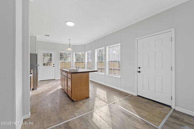 kitchen featuring sink, ornamental molding, stainless steel refrigerator, a center island with sink, and pendant lighting