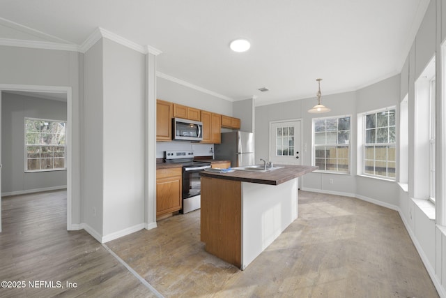 kitchen with decorative light fixtures, light wood-type flooring, a center island with sink, crown molding, and appliances with stainless steel finishes