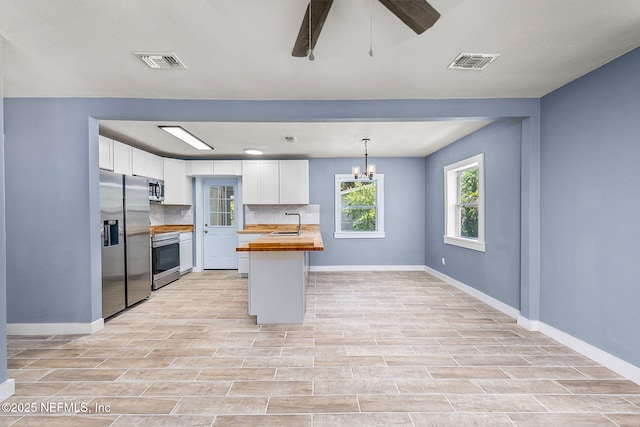 kitchen with wood counters, appliances with stainless steel finishes, decorative backsplash, hanging light fixtures, and white cabinets