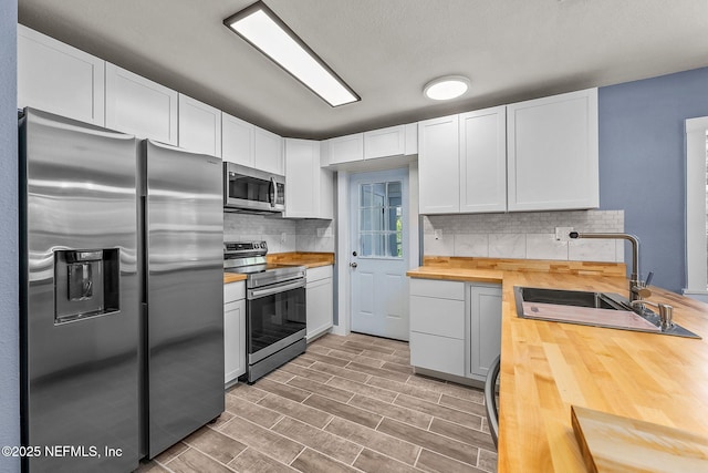 kitchen with wood counters, stainless steel appliances, tasteful backsplash, white cabinets, and sink