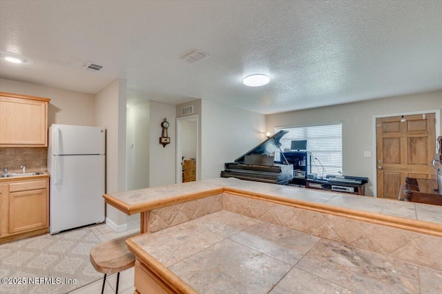 kitchen with light brown cabinets, tile counters, a breakfast bar area, and white fridge