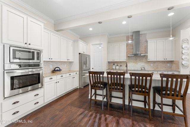 kitchen with appliances with stainless steel finishes, light stone counters, pendant lighting, wall chimney exhaust hood, and white cabinets