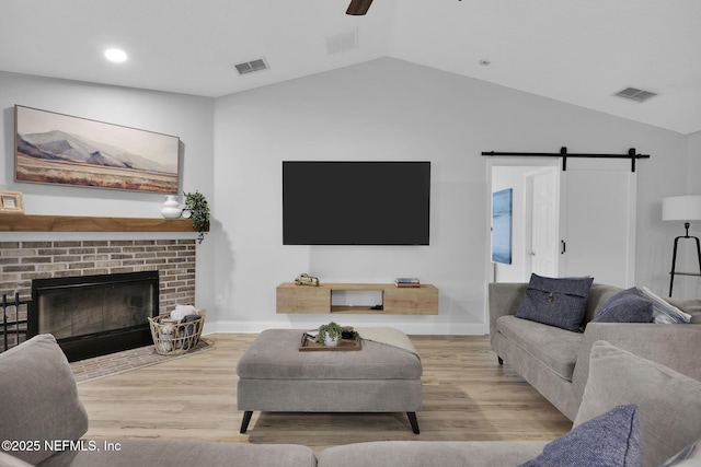 living room with light hardwood / wood-style flooring, lofted ceiling, a brick fireplace, a barn door, and ceiling fan