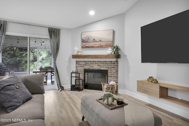 living room with light wood-type flooring, a brick fireplace, and vaulted ceiling