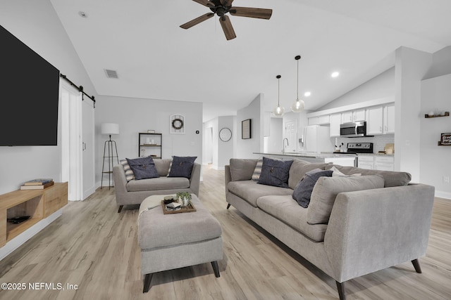 living room with ceiling fan, light hardwood / wood-style floors, a barn door, and lofted ceiling