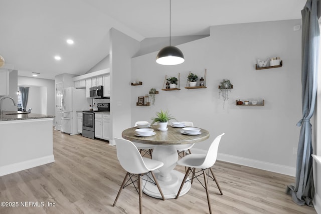 dining space featuring sink, light wood-type flooring, and vaulted ceiling