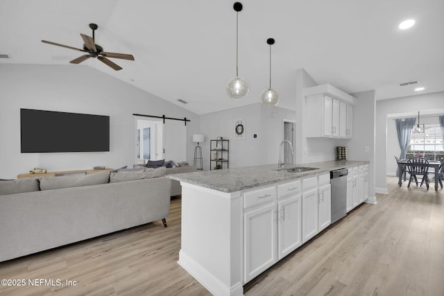 kitchen with sink, white cabinets, light stone counters, stainless steel dishwasher, and a barn door