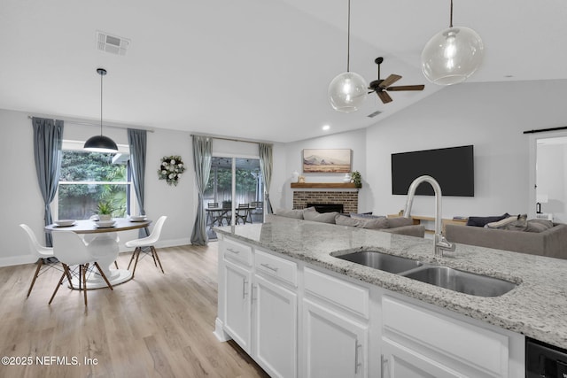 kitchen with decorative light fixtures, lofted ceiling, a brick fireplace, white cabinets, and sink