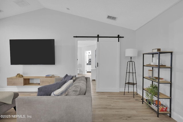 living room featuring light wood-type flooring, vaulted ceiling, and a barn door