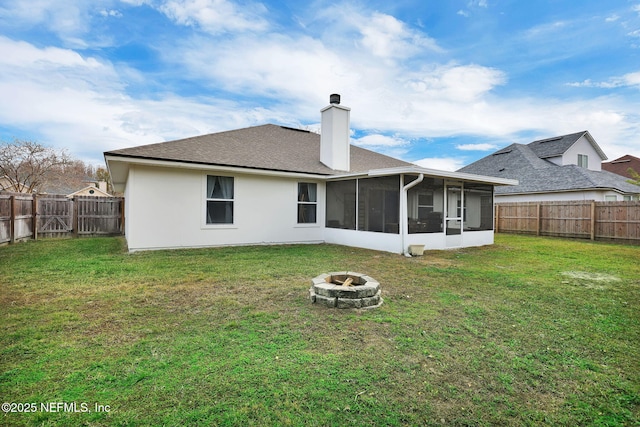 back of property with a sunroom, a yard, and a fire pit