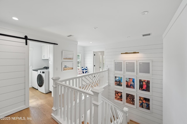 hallway featuring a barn door, wood walls, light wood-type flooring, and washer and clothes dryer