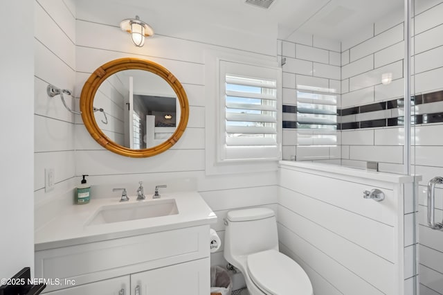 bathroom featuring vanity, wood walls, and toilet