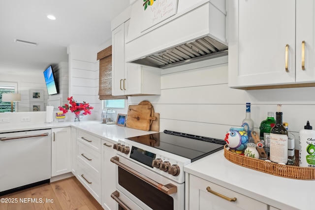 kitchen featuring white appliances, custom exhaust hood, white cabinets, and light wood-type flooring