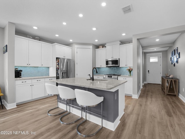 kitchen featuring light hardwood / wood-style floors, an island with sink, appliances with stainless steel finishes, white cabinets, and sink