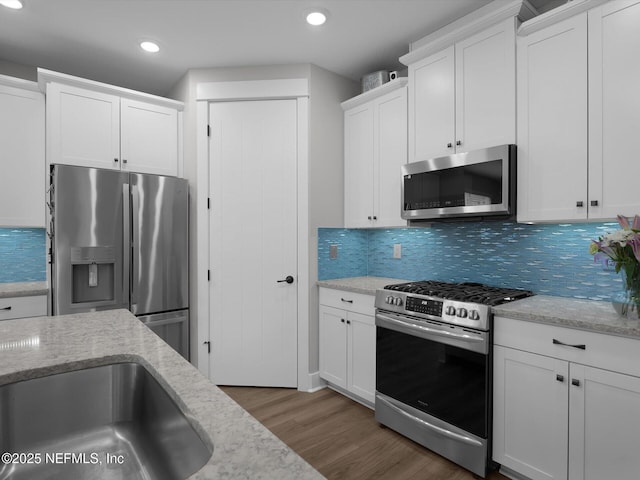 kitchen featuring stainless steel appliances, white cabinets, tasteful backsplash, and light stone countertops