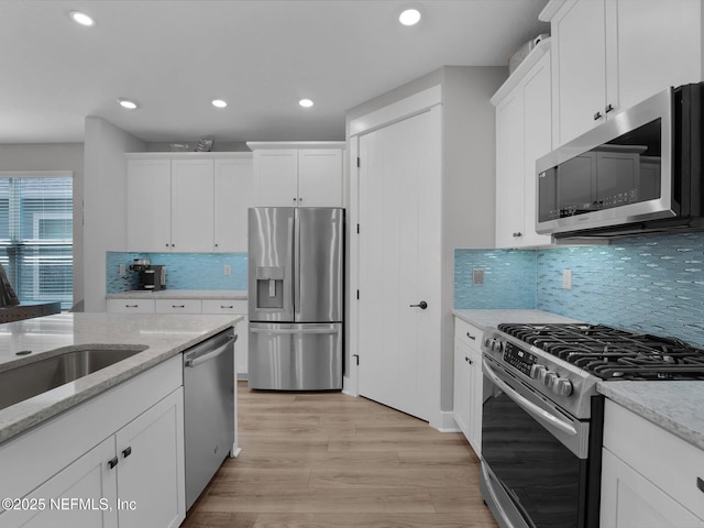 kitchen featuring light stone countertops, white cabinets, light hardwood / wood-style flooring, and stainless steel appliances